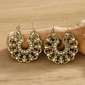 Macro shot of gold bohemian earrings with intricate hollow patterns on a wood surface