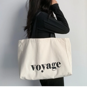 Detail view of large cream canvas tote bag with black VOYAGE lettering on shoulder