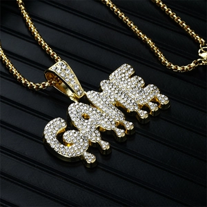 Gros plan du pendentif lettre GAME doré avec strass sur un fond texturé noir