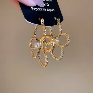 Golden flower hoop earrings with textured metal petals and a white pearl center