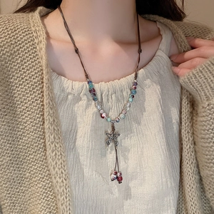 Close-up of ethnic beaded necklace with silver butterfly pendant on knit sweater
