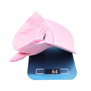 Pink cotton unicorn baseball cap for kids weighing 64g on a scale against a white background