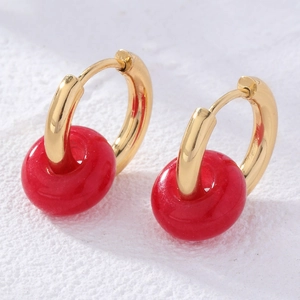 Detail view of gold hoop earrings with red donut-shaped natural stone pendants on white