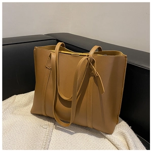 Detail view of large brown faux leather tote bag with dual shoulder straps on a sofa