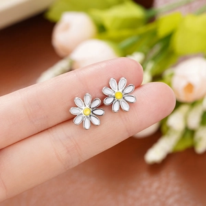Detailed close-up of small daisy flower stud earrings with white enamel petals and yellow core