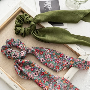 Close-up of olive green satin and floral print scrunchies with elegant long ribbons