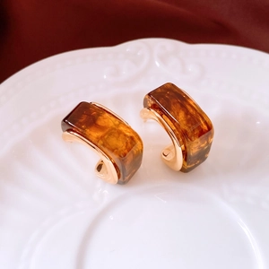 Detailed close-up of retro amber resin C-shape earrings on a white vintage ceramic plate