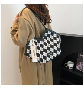On-shoulder view of large black and white checkered tote bag with fashion tag