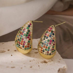 Pendientes de gota dorados de lujo con circonitas de colores en fondo de piedra