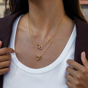 Close-up of layered paperclip chain necklaces with heart and interlocking rings pendants