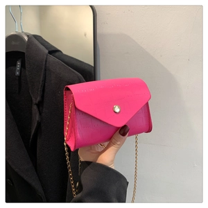 Detail of bright pink crocodile embossed envelope bag with gold clasp and chain strap