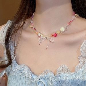 Colorful beaded necklace with white bow pendant worn by a model in soft lighting