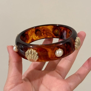 Macro view of tortoiseshell resin bangle featuring gold seashell and pearl embellishments