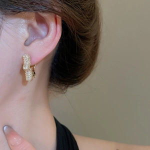 Close-up of gold zircon twisted star hoop earrings worn on a female model ear