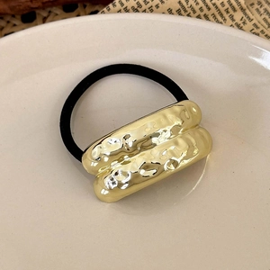 Close-up of golden hammered metal hair tie with black elastic band on ceramic plate