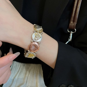 Macro detail of mixed metal stretch bracelet featuring embossed heart patterns and filigree