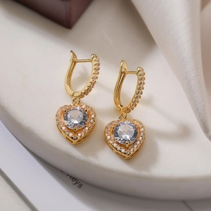 Elegant gold-plated heart earrings with round cubic zirconia on marble background