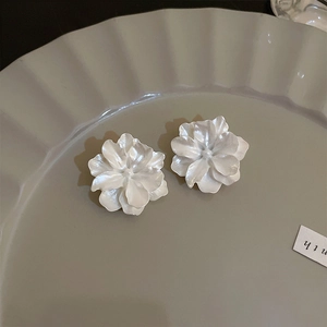 Detail of elegant white floral stud earrings on a textured plate with soft lighting
