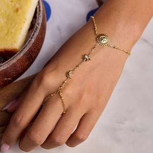 Elegant gold celestial hand chain with sun moon and star charms on a marble surface