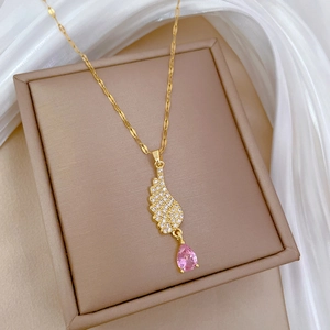 Macro detail of gold angel wing pendant with pink teardrop gem on beige jewelry box