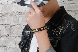 Detail of men's black and gold woven leather bracelet worn by a model in a urban setting