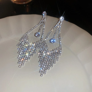 Close-up of sparkling silver tassel earrings with zircon crystals on a white ceramic plate
