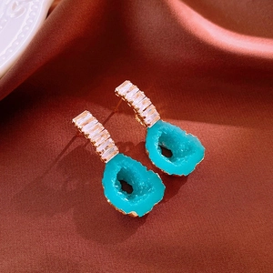 Detail of leaf earrings with gold finish and blue druzy stone on red satin background