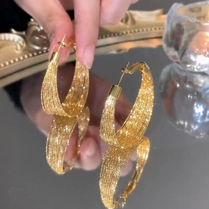 Macro detail of gold hoop earrings with woven texture and reflective mirror finish