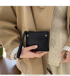 Close-up of black leather coin purse with gold zipper and wrist strap held by hand