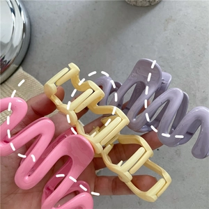 Close-up of pink, yellow and purple wavy plastic hair claw clips held in hand