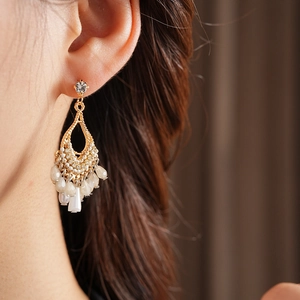 Detail of bohemian gold drop earrings with white beads and rhinestone tassels