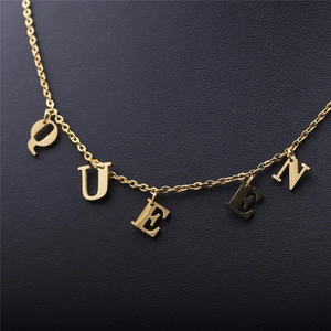 Close-up of golden QUEEN letter pendant on a fine chain over black leather background