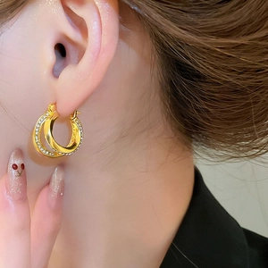 Side view detail of a model wearing double-layered golden hoop earrings with sparkling rhinestones