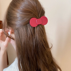 Close-up of matte red flower hairpin with embossed letter detail on a half-up hairstyle