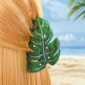Détail d'une pince à cheveux feuille verte avec strass sur cheveux avec fond de plage