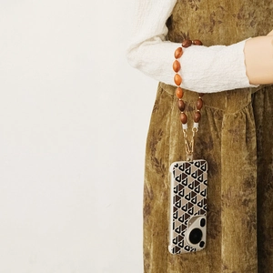 Détail de la dragonne de téléphone en perles de résine sur une robe marron d'automne