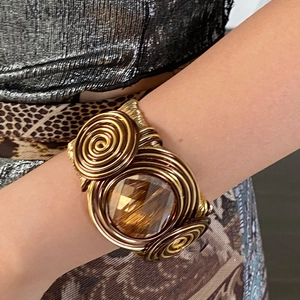 Close-up of twisted woven metal cuff bracelet featuring a large faceted amber crystal