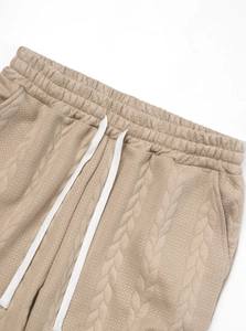 Detail of knitted khaki joggers showing elastic waist with white drawstring and cable texture