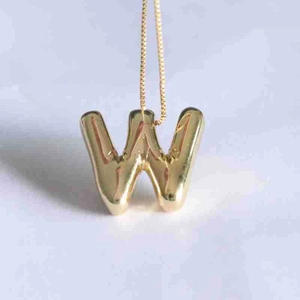 Polished golden bubble letter W pendant necklace with a mirror finish on textured background