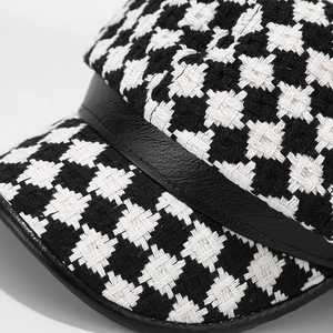 Detailed close-up of houndstooth tweed texture and black leather brim on baker boy hat