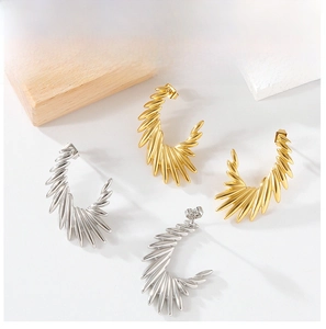 Close-up of wing-shaped C-style earrings in gold and silver with feather texture