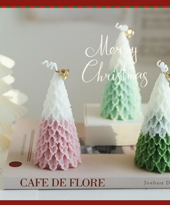 Close-up of geometric Christmas tree candles with golden bells on a book stand