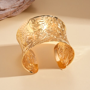 Detailed macro view of wide golden cuff bracelet with floral paisley relief patterns