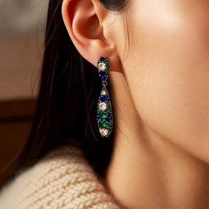 Detail view of vintage-style drop earrings with green and blue gemstones on a model