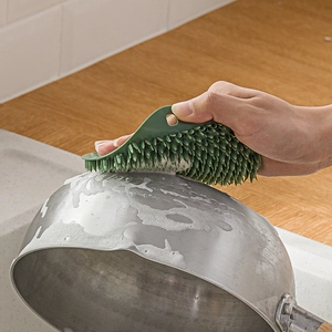Green silicone dish brush cleaning a soapy metal pan in a modern kitchen sink setting