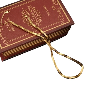 Irregular geometric gold snake chain necklace on a vintage red book with white background