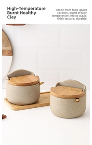 Detail of matte ceramic seasoning jars with wooden lids and spoons on a bamboo tray