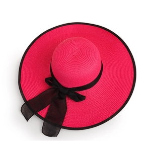 Close-up of magenta straw sun hat featuring a large brim and stylish black ribbon bow