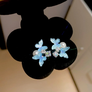 Blue resin butterfly stud earrings with zircon and pearl on black flower stand