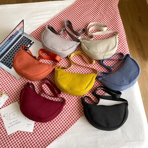 Flat lay of nylon crossbody dumpling bags in seven vibrant colors on checkered cloth